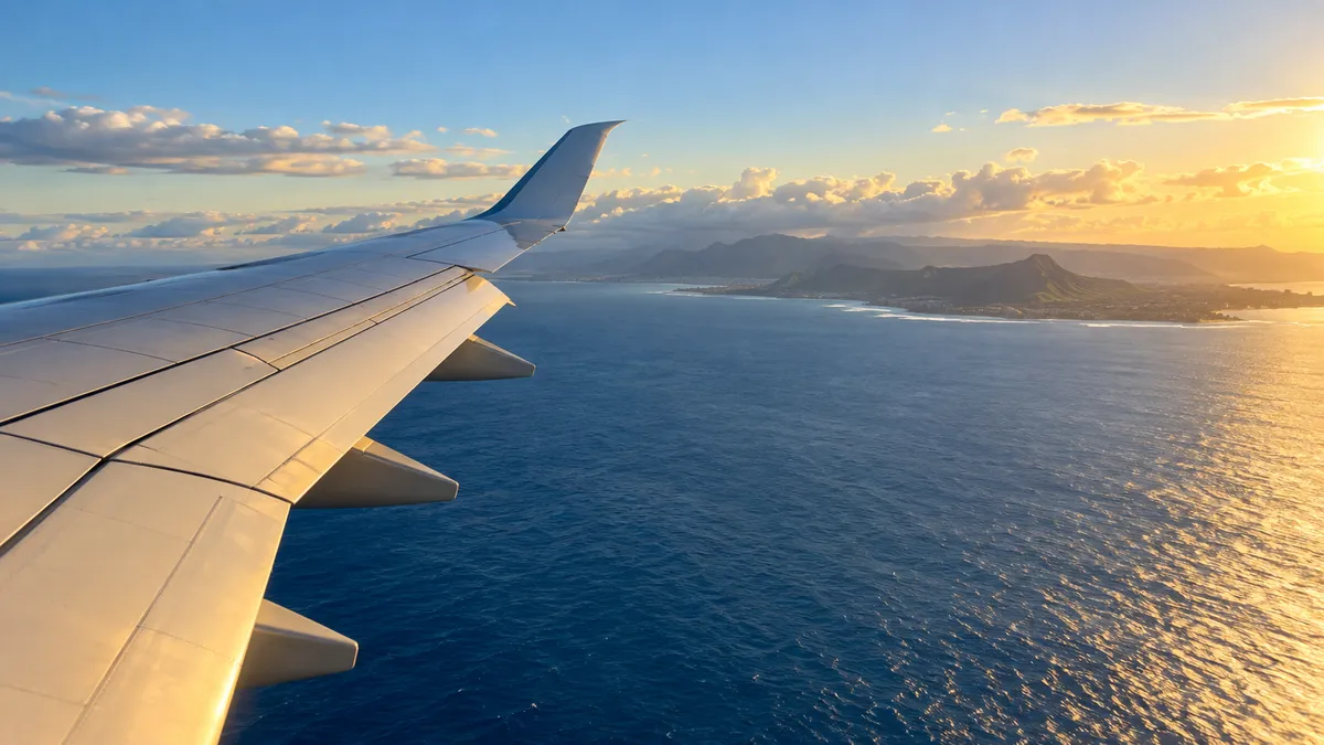 Generic illustration of a wide-body jet wing over blue Pacific water at golden hour with a hazy Oahu coastline below; not an image of the announced cabins, which do not exist yet