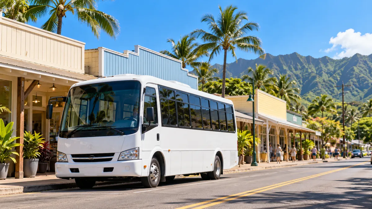 A white mid-size shuttle bus parked on a quiet small-town street lined with low wooden storefronts and palm trees, late-morning sun, North Shore Oahu feel, no people in focus